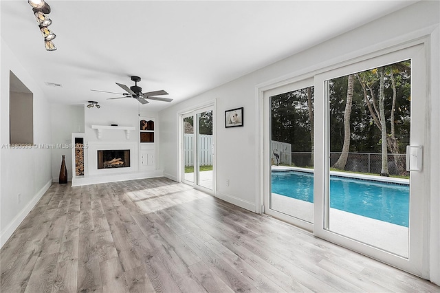 unfurnished living room featuring built in shelves, light wood-type flooring, a wealth of natural light, and ceiling fan