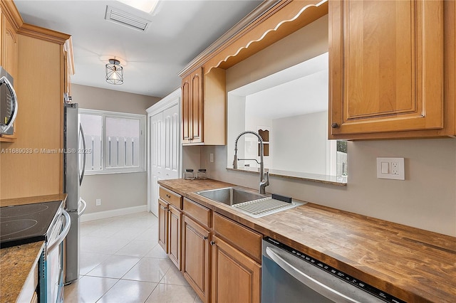 kitchen with wooden counters, light tile patterned floors, stainless steel appliances, and sink