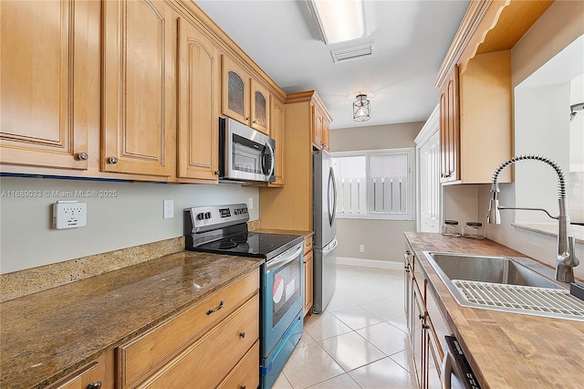 kitchen with light tile patterned flooring, stainless steel appliances, dark stone counters, and sink