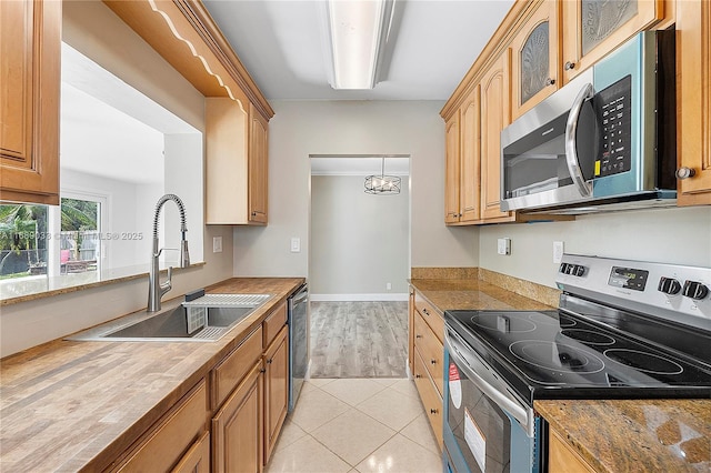 kitchen featuring appliances with stainless steel finishes, sink, light tile patterned floors, decorative light fixtures, and a chandelier