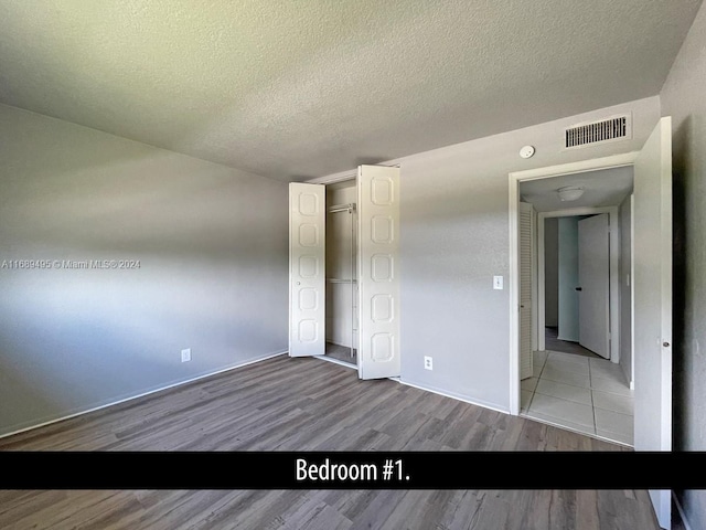 unfurnished bedroom featuring a textured ceiling, a closet, and light wood-type flooring