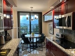 kitchen featuring black electric stovetop, decorative backsplash, a notable chandelier, light stone countertops, and decorative light fixtures