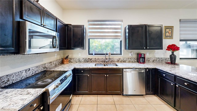 kitchen with light stone counters, sink, light tile patterned floors, and stainless steel appliances