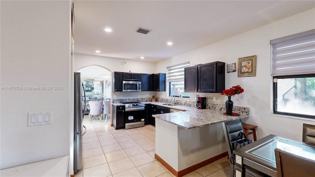 kitchen with stainless steel appliances, light stone counters, kitchen peninsula, sink, and a breakfast bar area