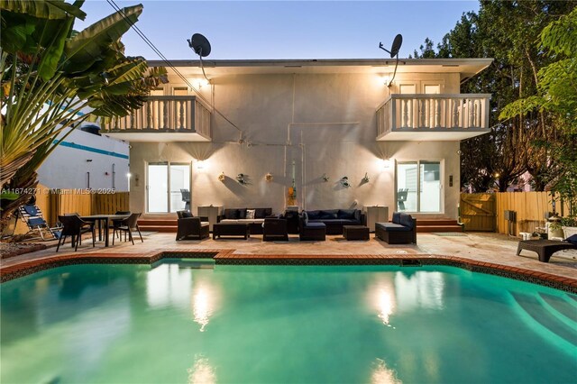 rear view of property featuring a fenced in pool, a patio, outdoor lounge area, and a balcony