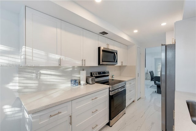 kitchen with light stone countertops, appliances with stainless steel finishes, decorative backsplash, and white cabinets