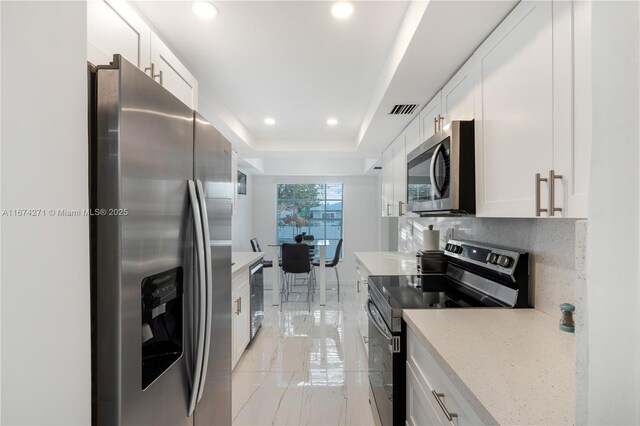 kitchen with stainless steel appliances, white cabinetry, a raised ceiling, and backsplash