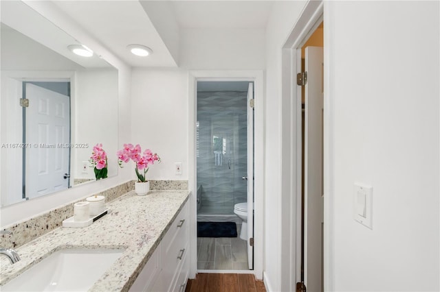 bathroom with hardwood / wood-style flooring, vanity, toilet, and a shower with door