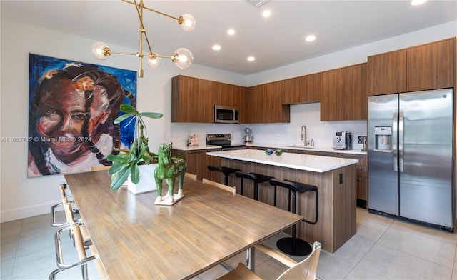 kitchen with sink, appliances with stainless steel finishes, decorative light fixtures, a chandelier, and a kitchen island