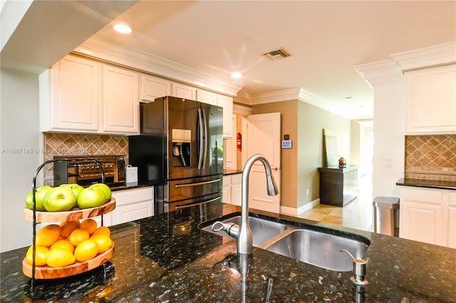 kitchen featuring refrigerator with ice dispenser, dark stone counters, sink, backsplash, and white cabinetry