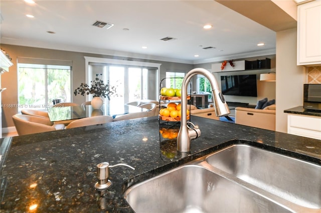 kitchen with white cabinets, a healthy amount of sunlight, crown molding, and dark stone countertops