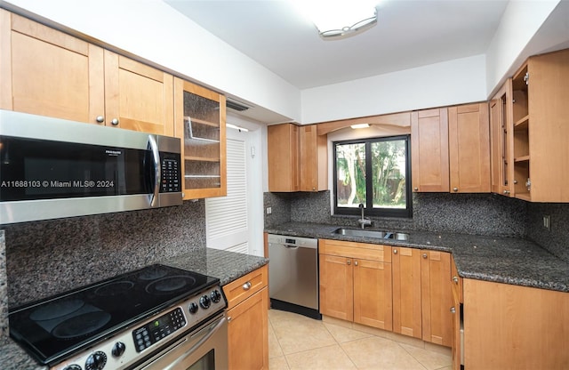 kitchen with sink, tasteful backsplash, dark stone countertops, light tile patterned flooring, and appliances with stainless steel finishes