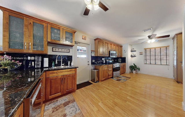 kitchen featuring stainless steel appliances, backsplash, sink, dark stone countertops, and light hardwood / wood-style flooring