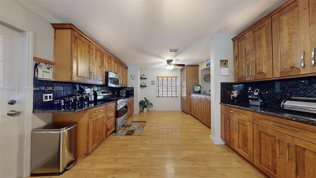 kitchen featuring stainless steel appliances, ceiling fan, dark stone countertops, light wood-type flooring, and decorative backsplash