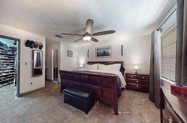 bedroom with ceiling fan, a textured ceiling, a walk in closet, and carpet