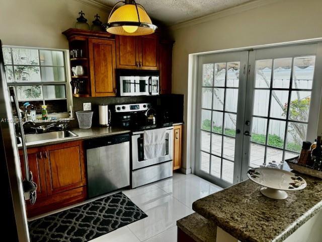 kitchen with french doors, crown molding, a textured ceiling, appliances with stainless steel finishes, and dark stone counters