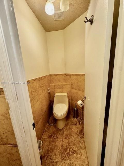 bathroom with toilet, a textured ceiling, and tile walls