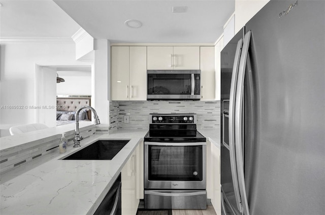 kitchen featuring appliances with stainless steel finishes, ornamental molding, light stone counters, decorative backsplash, and sink