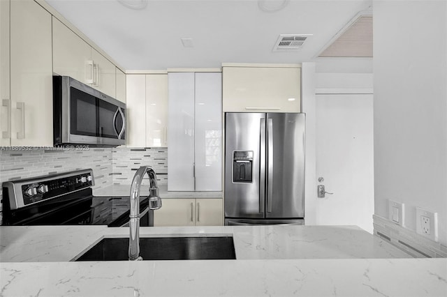 kitchen with sink, backsplash, light stone counters, and appliances with stainless steel finishes