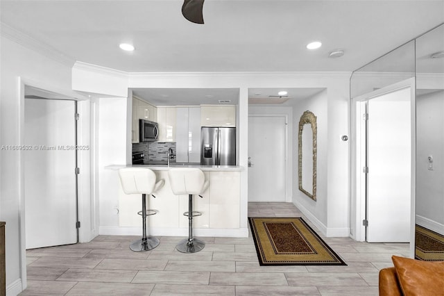 kitchen featuring kitchen peninsula, white cabinetry, appliances with stainless steel finishes, ornamental molding, and a kitchen breakfast bar