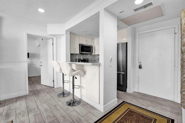 kitchen featuring white cabinetry, a kitchen bar, ornamental molding, decorative backsplash, and appliances with stainless steel finishes