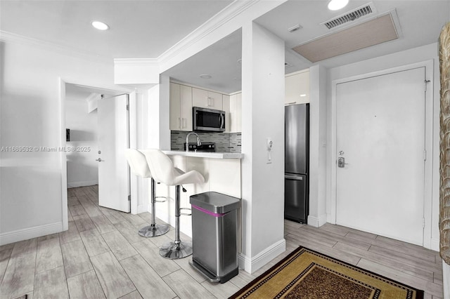 kitchen with stainless steel appliances, crown molding, a breakfast bar, decorative backsplash, and white cabinetry