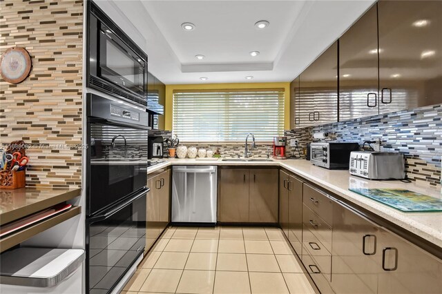 kitchen with decorative backsplash, black appliances, sink, light tile patterned floors, and a tray ceiling