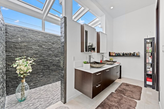 bathroom with tile patterned floors, a towering ceiling, vanity, a shower, and a skylight