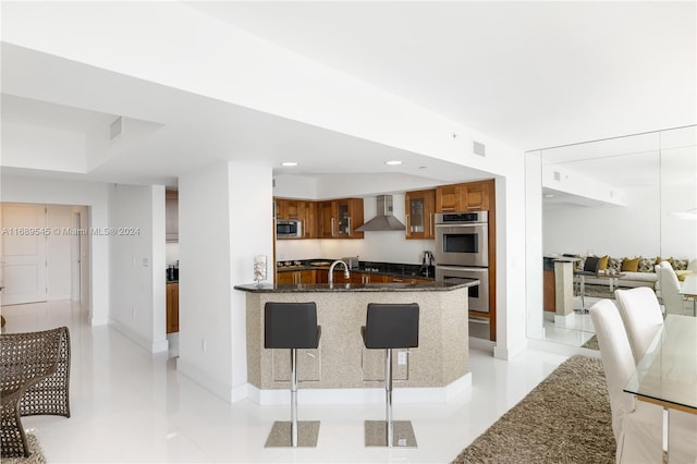 kitchen featuring appliances with stainless steel finishes, light tile patterned floors, sink, dark stone countertops, and wall chimney exhaust hood