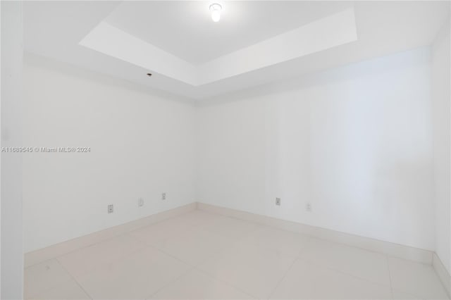 tiled empty room featuring a tray ceiling