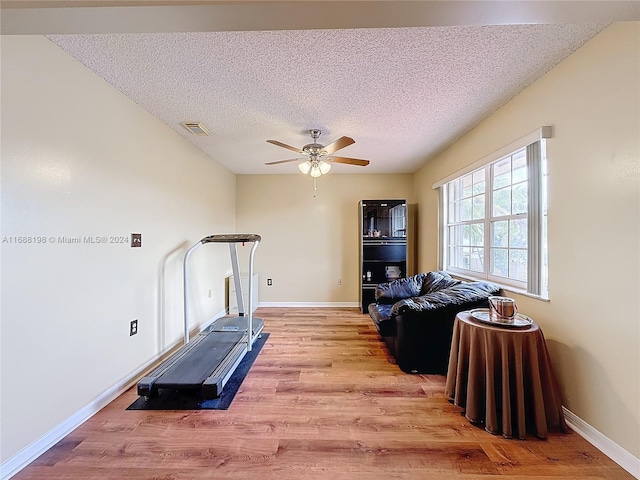 exercise area featuring a textured ceiling, light hardwood / wood-style flooring, and ceiling fan