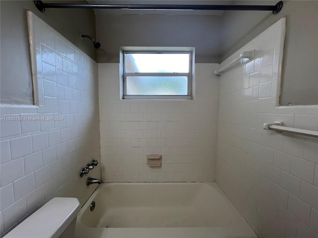 bathroom featuring toilet, tiled shower / bath combo, and tile walls