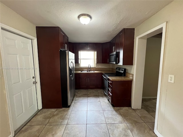 kitchen with appliances with stainless steel finishes, sink, light tile patterned floors, and a textured ceiling