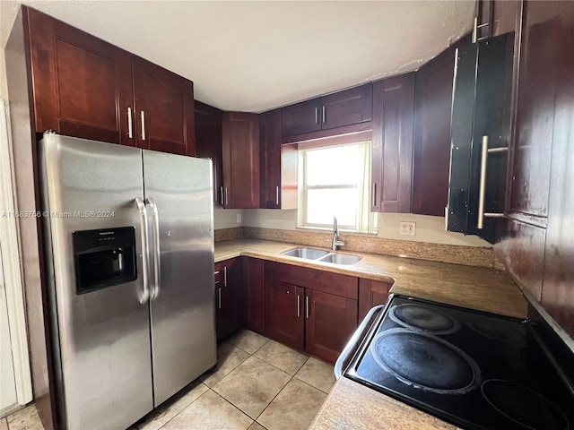 kitchen featuring light tile patterned floors, stainless steel refrigerator with ice dispenser, sink, and black range oven