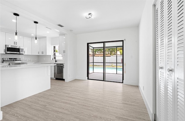 kitchen with appliances with stainless steel finishes, hanging light fixtures, light wood-type flooring, decorative backsplash, and white cabinets