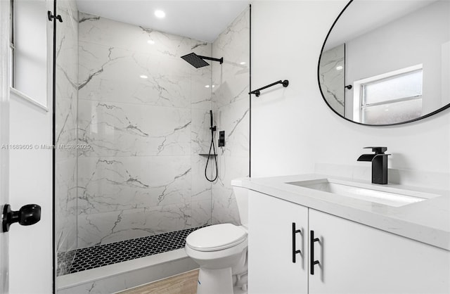 bathroom featuring hardwood / wood-style flooring, a tile shower, vanity, and toilet