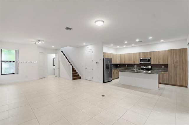 kitchen featuring a center island with sink, backsplash, light tile patterned floors, and stainless steel appliances