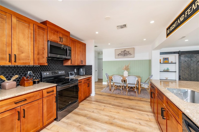 kitchen featuring tasteful backsplash, appliances with stainless steel finishes, a barn door, light stone countertops, and light hardwood / wood-style floors