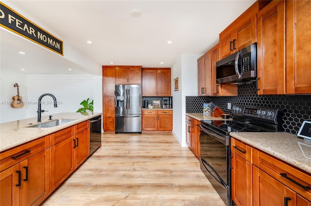 kitchen with black appliances, light wood-type flooring, sink, and light stone counters