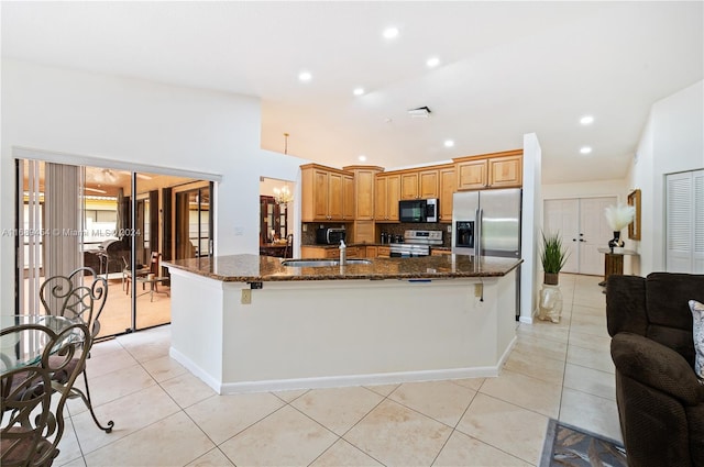 kitchen featuring stainless steel appliances, dark stone counters, a large island with sink, and a breakfast bar