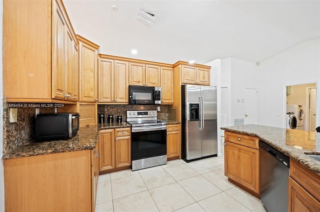 kitchen with dark stone countertops, vaulted ceiling, decorative backsplash, appliances with stainless steel finishes, and independent washer and dryer