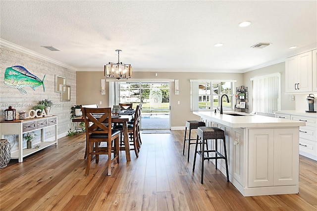 dining area with a notable chandelier, a textured ceiling, sink, crown molding, and light hardwood / wood-style flooring