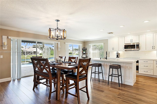 dining space with wood-type flooring, a chandelier, sink, and ornamental molding