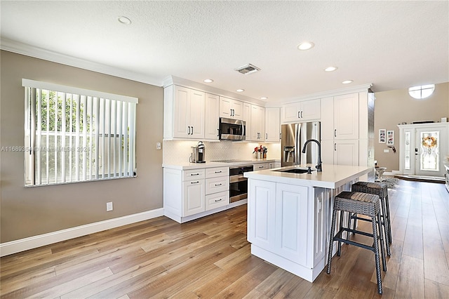 kitchen featuring appliances with stainless steel finishes, an island with sink, a kitchen breakfast bar, white cabinets, and light hardwood / wood-style flooring