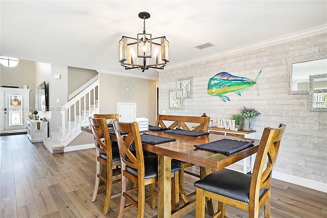 dining room with hardwood / wood-style flooring, wooden walls, crown molding, and a notable chandelier