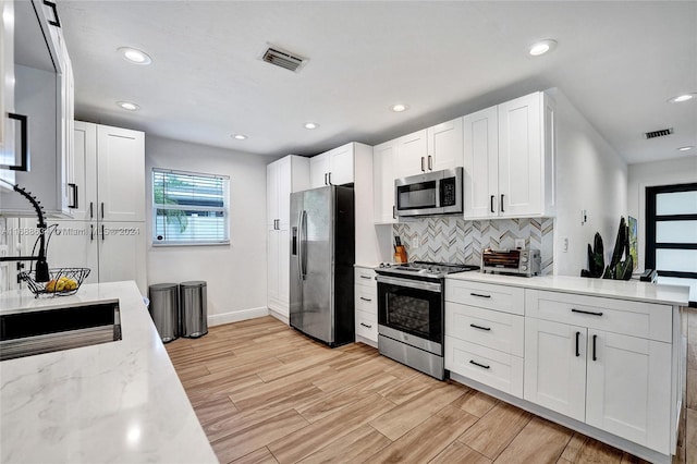 kitchen with stainless steel appliances, light stone counters, white cabinets, backsplash, and light hardwood / wood-style flooring