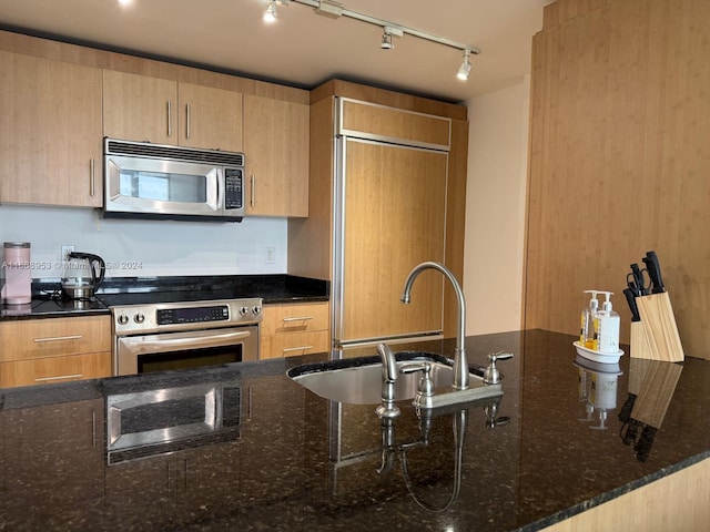 kitchen with stainless steel appliances, track lighting, sink, light brown cabinetry, and dark stone countertops