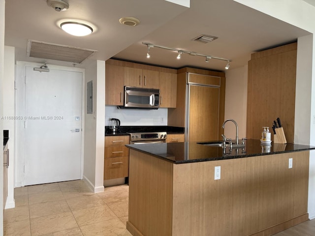 kitchen with sink, kitchen peninsula, appliances with stainless steel finishes, dark stone counters, and electric panel