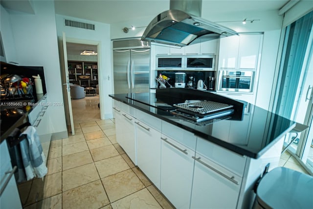 kitchen with stainless steel appliances, white cabinetry, island range hood, light tile patterned floors, and a kitchen island