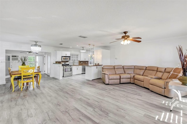 living room featuring ceiling fan, a textured ceiling, and light wood-type flooring